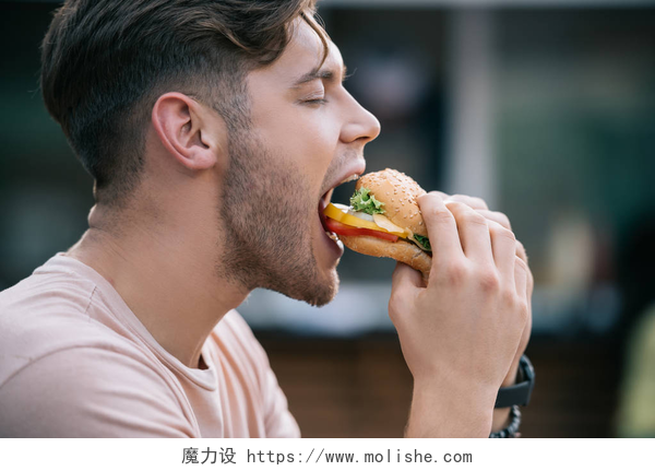 一个男人在吃着美味汉堡人吃可口的汉堡与闭着眼睛的侧面看法